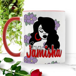 May include: White ceramic mug with a red handle. The mug features a black and white illustration of a woman with long black hair and a red hoop earring. The mug has a purple floral pattern and the name "Jamisha" written in red and gray letters.