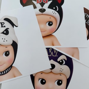 Può includere: Tre cartoline stampate con illustrazioni di figure simili a neonati che indossano cappelli a tema animale. Un cappello è bianco con il muso di un bulldog nero e la lettera E, un altro è nero con un cane dalle orecchie rosse e le lettere BU, e il terzo è viola con il muso di un cane e la lettera W.