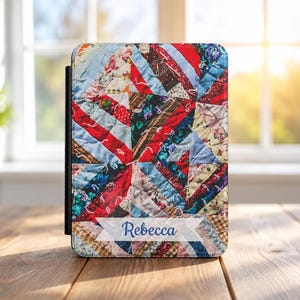 May include: A rectangular e-reader case featuring a colorful patchwork quilt pattern with various fabric textures and prints in shades of red, blue, and white. A white banner across the bottom displays the name Rebecca in blue script lettering.