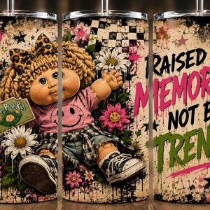 May include: A cylindrical tumbler featuring a Cabbage Patch Kids doll with blonde yarn hair and a leopard print bow. The design includes a pink smiley face shirt, denim shorts, and black sneakers, surrounded by daisies, stars, and the text RAISED BY MEMORIES NOT BY TRENDS.