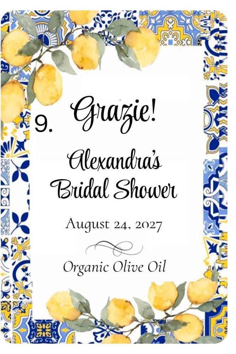 Puede incluir: Una tarjeta blanca con un borde decorativo con limones amarillos y patrones de azulejos azules y amarillos. La tarjeta dice "Grazie! Alexandra's Bridal Shower August 24, 2027 Organic Olive Oil."