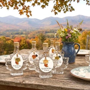 May include: A white ceramic mug with a black handle and the text "But First, Coffee" in a bold, black font. The mug is set against a blurred background, suggesting a cozy setting.