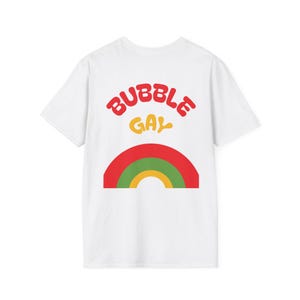May include: A white short-sleeved t-shirt featuring a graphic on the back. The text BUBBLE GAY is printed in red and yellow with a wavy font. Below the text is a semi-circular rainbow graphic composed of red, green, and yellow bands.