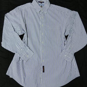Puede incluir: Una camisa de manga larga con botones y un patrón de rayas verticales en blanco y azul marino. La camisa incluye un cuello puntiagudo, una tapeta de botones frontal y un bolsillo en el pecho. La etiqueta de Tommy Hilfiger es visible en el cuello.
