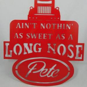 May include: A red metal sign in the shape of a semi-truck. The sign reads "AIN'T NOTHIN' AS SWEET AS A LONG NOSE Pete". The sign is cut out with the words and truck details visible.