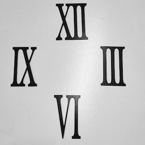 May include: Four individual black Roman numerals representing the numbers twelve, three, six, and nine, arranged in a cross formation. Each numeral features a bold, serif typeface and a flat, matte finish, designed for wall mounting or display.