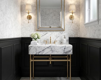 May include: A white marble bathroom vanity with a gold metal frame, featuring a rectangular basin, gold faucet, and matching gold-framed mirror. The vanity is flanked by two wall-mounted lamps with beige shades, set against black wainscoting.