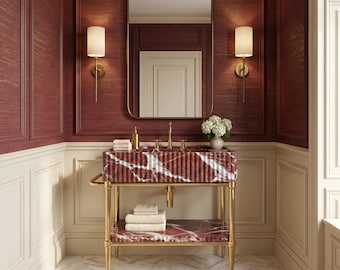 May include: A bathroom vanity featuring a fluted red marble sink basin and a matching lower shelf supported by a gold metal frame. The vanity includes a gold faucet, a rectangular mirror, two wall sconces, and stacked white towels.