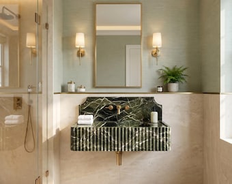 May include: A wall-mounted bathroom sink crafted from dark green marble with a fluted front design. The sink features a matching marble backsplash, gold-toned hardware, and is positioned beneath a rectangular mirror with a gold frame and two wall sconces.