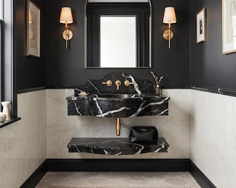 May include: A bathroom vanity featuring a black marble sink and matching shelf with gold hardware. Above the sink is an arched mirror flanked by two gold wall sconces. The walls are painted black with white marble wainscoting and black trim.