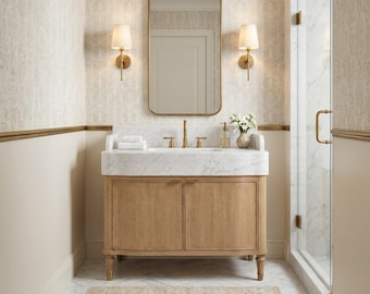 May include: A bathroom vanity with a light wood cabinet, a white marble countertop, and a gold faucet. Above the vanity is a rectangular mirror flanked by two gold wall sconces. A small vase with white flowers sits on the marble surface.