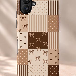 May include: A smartphone case featuring a patchwork design in shades of brown, beige, and cream. The pattern consists of alternating squares decorated with small bows, polka dots, vertical stripes, and tiny hearts, creating a grid-like aesthetic.