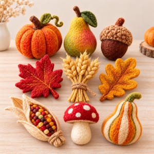 Puede incluir: Una colección de decoraciones de otoño de lana fieltrada que incluye una calabaza naranja, una pera, una bellota, una hoja de arce roja, una gavilla de trigo, una hoja de roble, una mazorca de maíz, una seta roja y blanca y una calabaza rayada.