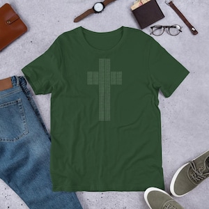 Puede incluir: Una camiseta de manga corta en color verde bosque oscuro con un gráfico central de una cruz compuesta por dígitos de código binario repetidos. El diseño está impreso en color gris claro, creando una estética digital sobre la tela lisa.