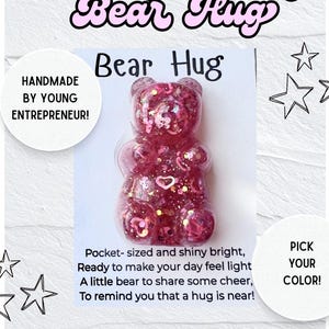 May include: A pink resin bear figurine with embedded glitter and heart-shaped sequins attached to a card. The card features the text "Bear Hug" and a poem, with additional text stating "Custom Pocket Bear Hug", "HANDMADE BY YOUNG ENTREPRENEUR!", and "PICK YOUR COLOR!" alongside star graphics.