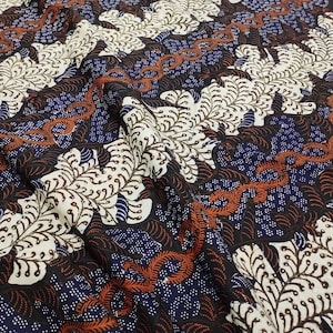 May include: A fabric featuring a batik pattern with large cream-colored leaf motifs, dark blue sections filled with small white dots, and winding orange vine-like elements. The textile displays a dense, repeating design with intricate details.