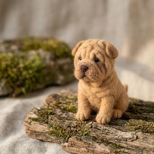 May include: A needle-felted Shar-Pei puppy figurine with a tan, textured wool coat, deep facial wrinkles, small dark eyes, and a dark brown nose. The puppy is sitting in an upright position, showcasing detailed craftsmanship and soft, fuzzy fur.