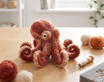 Op de afbeelding: Een naaldgevilte octopussculptuur gemaakt van gemêleerde roestkleurige, bruine en crèmekleurige wolvezels. De octopus heeft een ronde kop, twee opvallende ogen en acht gekrulde tentakels met zichtbare crèmekleurige zuignapdetails.