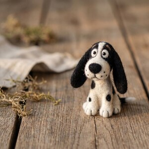 Könnte beinhalten: Eine nadelgefilzte Hundefigur mit weißem Körper, schwarzen Flecken und langen schwarzen Ohren. Der Hund hat eine schwarze Nase, dunkle Augen und eine texturierte Wolloberfläche. Er sitzt aufrecht und zeigt ein detailliertes Gesicht mit kleinen Schnurrhaaren.