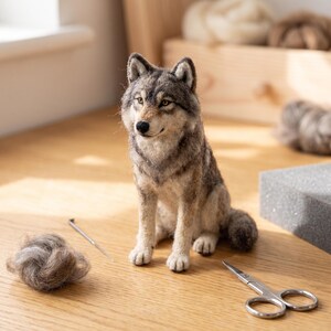 May include: A needle-felted wolf figurine crafted from gray, brown, and white wool fibers. The wolf is in a seated position with alert ears, amber-colored eyes, and a black nose. A small tuft of loose wool, a felting needle, and scissors are nearby.
