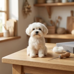 May include: A needle-felted white dog figurine with soft, textured fur, dark eyes, and a black nose. The small sculpture sits upright on a wooden surface next to a wooden-handled felting needle and a small tuft of white wool roving material.
