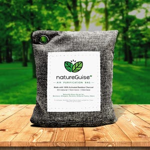 Op de afbeelding: Een rechthoekige grijze jute luchtzuiveringszak met een metalen oogje in de linkerbovenhoek. Een wit label bevat een groen bladlogo, de tekst natureGuise AIR PURIFICATION BAG en details over de inhoud van actieve bamboehoutskool.