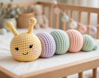 May include: A crocheted caterpillar toy featuring a yellow head with two antennae, black embroidered eyes, and pink cheeks. The body consists of four rounded segments in alternating pastel colors of lavender, mint green, peach, and light green.