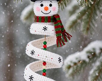 May include: A crocheted snowman ornament featuring a black top hat with holly, a red and green striped scarf, and a white spiral body decorated with black embroidered snowflakes and small red dots, finished with a white crocheted ball at the base.