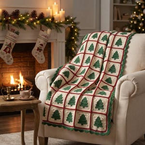 May include: A crochet blanket featuring a grid of cream-coloured squares, each containing a green Christmas tree motif. The squares are joined by dark red yarn, and the blanket is finished with a scalloped green border draped over a chair.