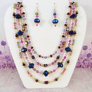 May include: A multi-strand necklace with gold chain and pink, purple, and blue crystal beads. Matching earrings with blue crystal beads.