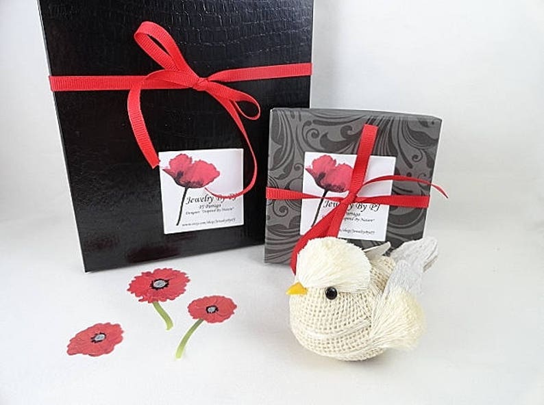May include: Two black gift boxes with red ribbon and a small white bird figurine. The boxes have a label that says "Jewelry by J" and a red poppy flower design.