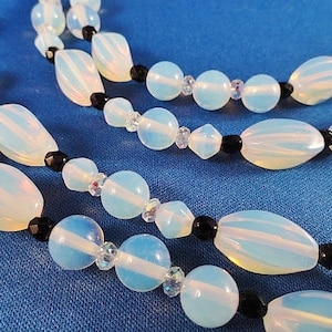 May include: A multi-strand necklace with white opal beads and black beads. The necklace is on a blue background.