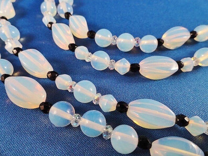 May include: A multi-strand necklace with white opal beads and black beads. The necklace is on a blue background.