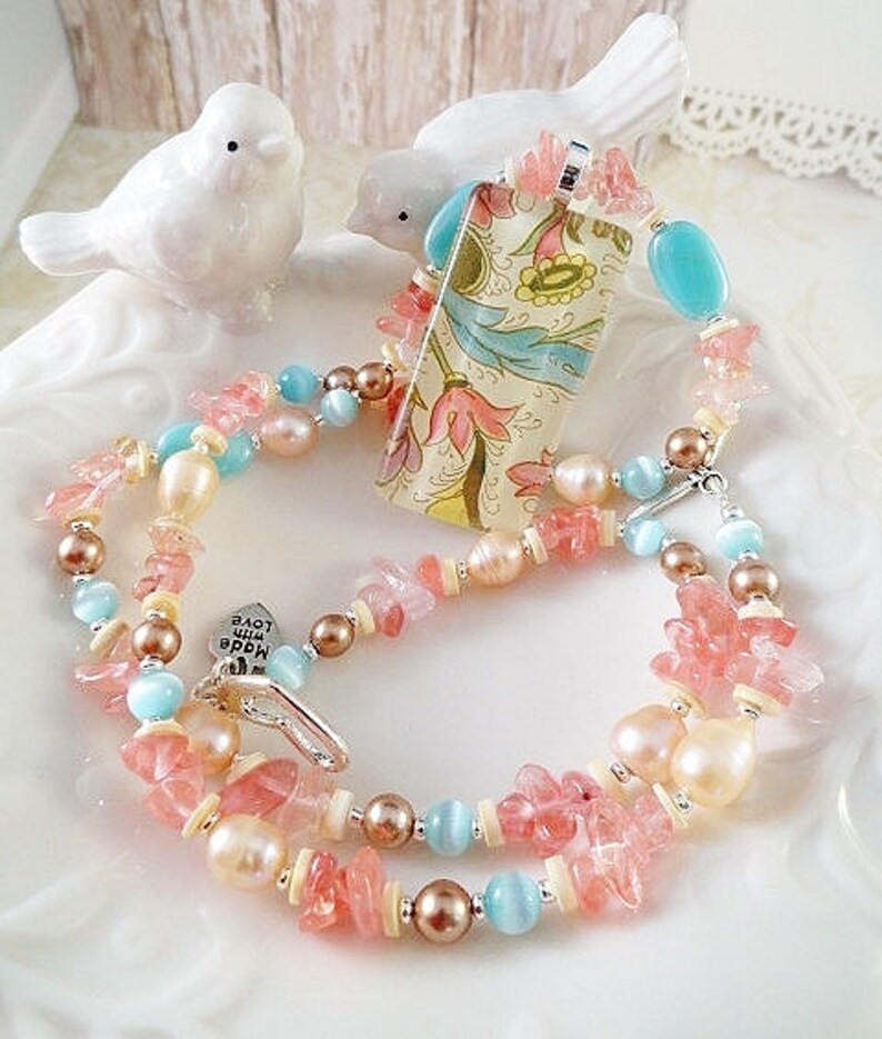May include: A multi-strand necklace with pink and blue beads, a floral patterned pendant, and a charm that says "Love the World".