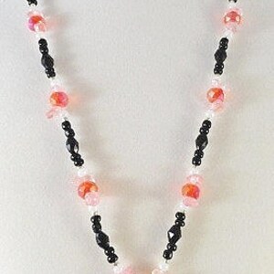 May include: A black and pink beaded necklace with a rectangular pendant featuring a floral design. The pendant is made of glass and has a pink, white, and green floral pattern.
