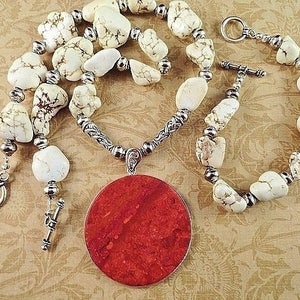 May include: A white and brown stone necklace with a large red pendant. The necklace has a silver chain and toggle clasp.