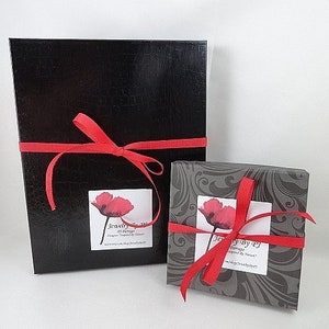 May include: Two black gift boxes with red ribbon and a poppy flower design on the label. The label reads "Jewelry by Design" and "Inspired by Nature".