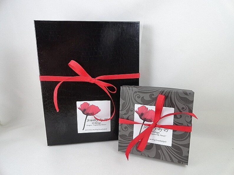 May include: Two black gift boxes with red ribbon and a poppy flower design on the label. The label reads "Jewelry by Design" and "Inspired by Nature".