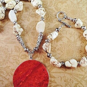 May include: A white howlite stone necklace and bracelet set with silver accents. The necklace features a large, round, red coral pendant.