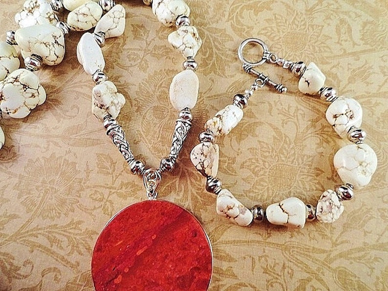 May include: A white howlite stone necklace and bracelet set with silver accents. The necklace features a large, round, red coral pendant.