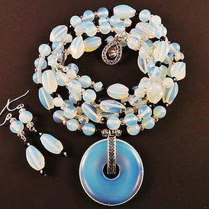 May include: A blue and white opal necklace with a large pendant and matching earrings. The necklace is made of multiple strands of beads and features a silver clasp.