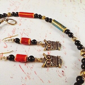 May include: A necklace and earrings set featuring owl charms, black beads, and red and blue ceramic beads.