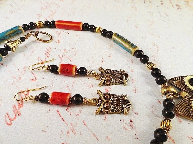 May include: A necklace and earrings set featuring owl charms, black beads, and red and blue ceramic beads.