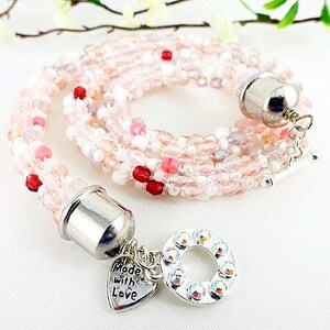 May include: A multi-strand beaded necklace in shades of pink, white, and red. The necklace features a silver clasp and a charm that says "Made with Love". The necklace is approximately 18 inches long.