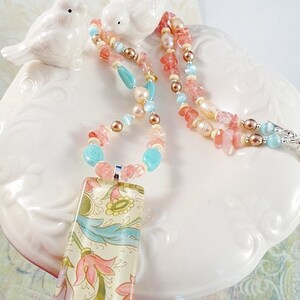 May include: A multi-strand necklace with pink, peach, and turquoise beads and a rectangular pendant with a floral pattern.