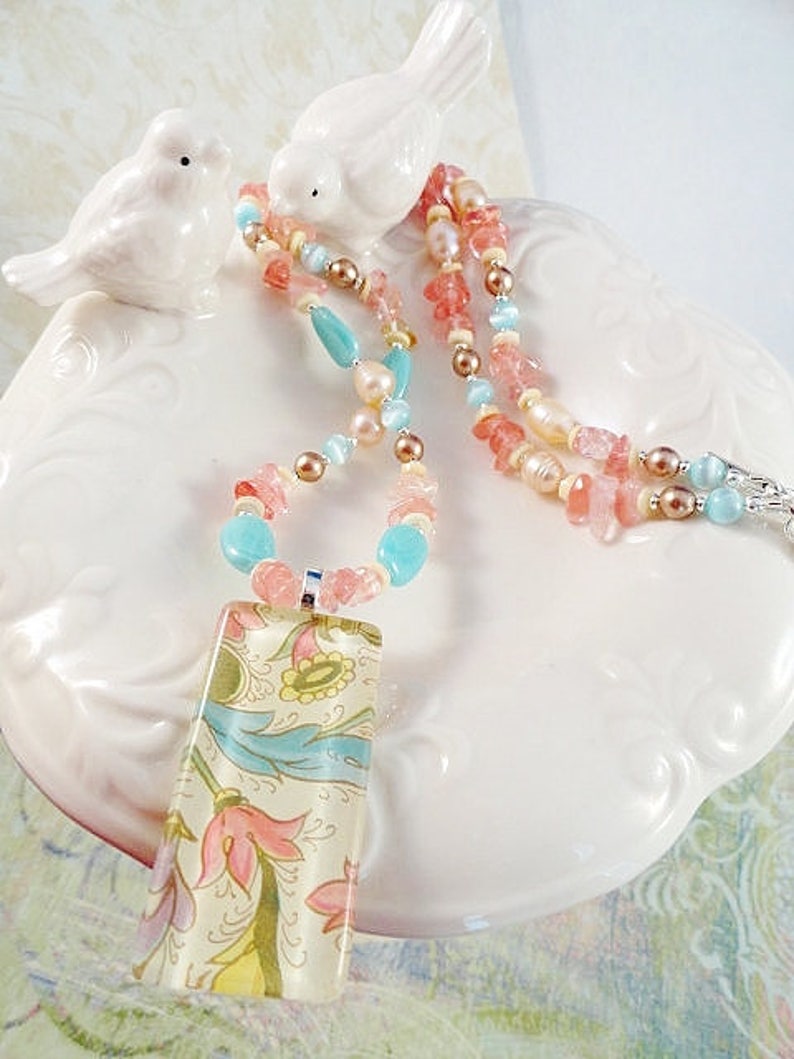 May include: A multi-strand necklace with pink, peach, and turquoise beads and a rectangular pendant with a floral pattern.