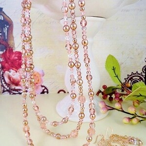 K&ouml;nnte beinhalten: Eine mehrreihige Halskette und ein passendes Ohrring-Set mit ros&eacute;goldenen und klaren Glasperlen. Die Halskette ist mit drei Perlenreihen geschichtet, und die Ohrringe sind im H&auml;nge-Stil mit mehreren Perlen.
