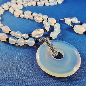 May include: A white opal necklace and earrings set with a silver pendant. The necklace features white opal beads and black beads. The pendant is a round opal with a silver design.