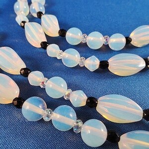 May include: A multi-strand necklace with white opal beads and black beads. The necklace is on a blue background.