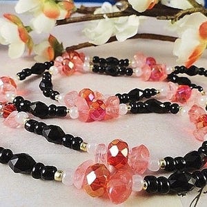 May include: A multi-strand necklace with black beads, pink and red faceted beads, and silver clasp.